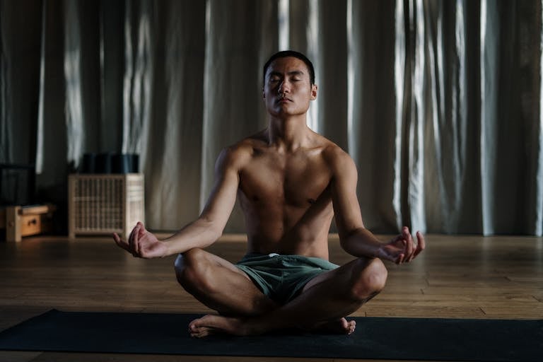 Shirtless asian man practicing yoga in meditation pose at home for wellness.