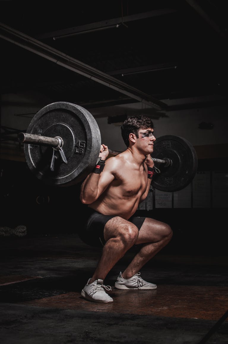 Shirtless man performing a barbell squat, showcasing strength and fitness.